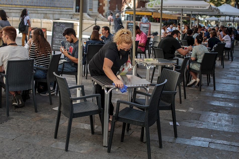Una camarera desinfecta una mesa de una terraza en el centro de Valencia
